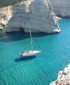 a sailboat floating in the blue water near cliffs