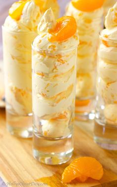 three glasses filled with dessert sitting on top of a wooden table next to an orange slice