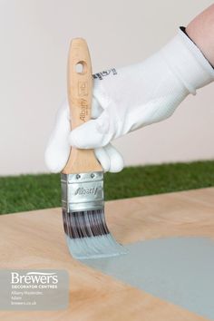 a person holding a paint brush on top of a wooden table with grass in the background