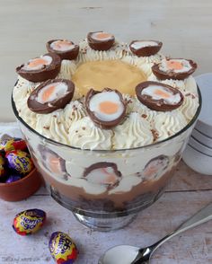 there is a cake in the glass bowl with chocolate eggs on top and white frosting