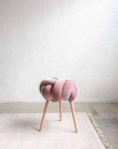 a pink chair sitting on top of a rug in front of a white wall and wooden legs