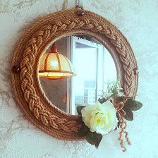 a roped mirror hanging on the wall next to a window with flowers in it