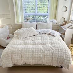 a bed with white comforters and pillows in a bedroom next to a window,