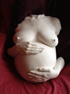 a pregnant woman's body is covered in white plaster on a red blanket, with her hands resting on the belly