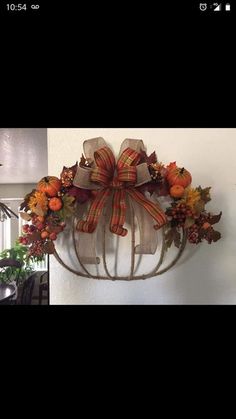 a wreath hanging on the side of a wall with fall decorations and bows attached to it