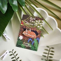 a red fox enamel pin sitting on top of a white plate next to green plants