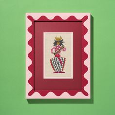 a red and white frame holding a cross - stitch picture on a green wall with scalloped edges