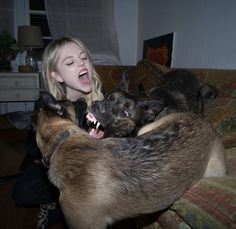 a woman is playing with two dogs on the couch in front of her, one dog has it's mouth open