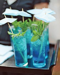 three glasses filled with blue liquid and mint sprigs on top of a table