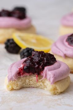 some cookies with pink frosting and blueberries on top are next to lemon slices