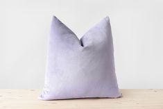 a lavender colored pillow sitting on top of a wooden table next to a white wall