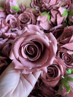 a person's hand holding a pink rose in the middle of a bouquet of purple flowers