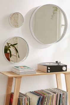 three circular mirrors on the wall above a wooden table with record players and records in front of it