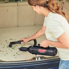 a woman is using a vacuum to clean the back of a car's trunk