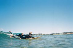 two people in wetsuits on surfboards paddling through the ocean water,