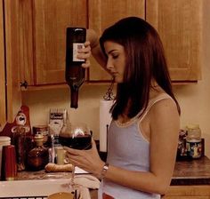 a woman standing in front of a kitchen counter holding a glass of wine and looking at her cell phone