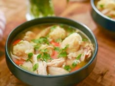 a bowl of chicken noodle soup on a wooden table with another bowl in the background