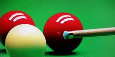 two red balls and a yellow ball with a wooden stick in front of them on a green surface