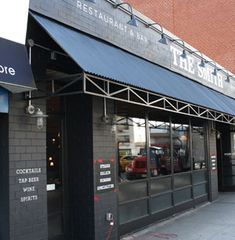 the exterior of a restaurant with awnings and black brick walls, on a city street