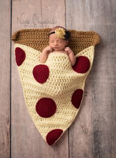 a baby wrapped in a blanket with red and white polka dots is laying on a wooden floor