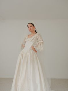 a woman in a white wedding dress standing with her hands on her hips and looking off to the side