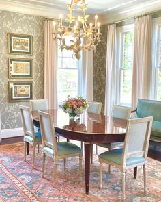 a dining room table with chairs and a chandelier hanging from the ceiling in front of two windows