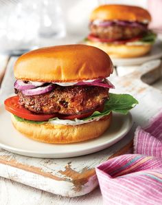 two burgers with lettuce, tomato and onion on a white platter