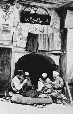 three men sitting on the ground in front of a building with an arabic sign above it