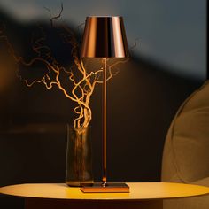 a table with a lamp on it next to a chair and a tree in the background