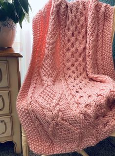 a pink knitted blanket sitting on top of a chair next to a potted plant