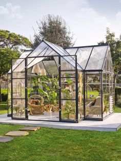 a small greenhouse in the middle of a grassy area with lots of plants inside it