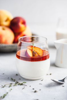 a glass filled with liquid next to some peaches and other fruit on the table