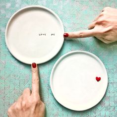 two white plates with red hearts on them, one pointing at the plate and the other pointing