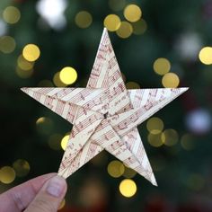 a hand holding up a paper origami star in front of a christmas tree