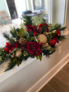 a window sill decorated with red and gold flowers, pine cones, greenery and ornaments