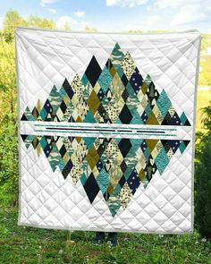 a quilted wall hanging in the grass with trees in the background and blue sky