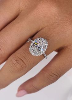 a woman's hand with a diamond engagement ring on her left hand and the center stone is surrounded by diamonds