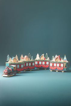 a toy train with houses and trees on the top is sitting in front of a blue background