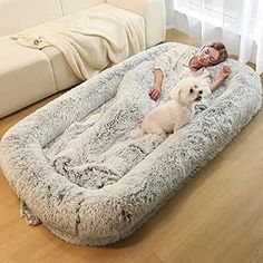 a woman laying on top of a dog bed with a white dog sitting next to her