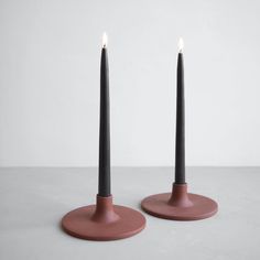 two black candles sitting on top of each other in front of a white wall and floor