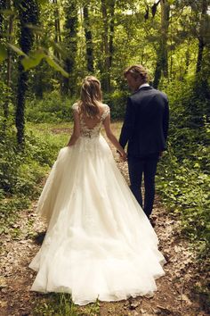 a bride and groom are walking through the woods holding hands while looking at each other