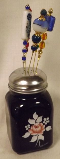 a blue jar with some pins sticking out of it's top and flowers on the bottom