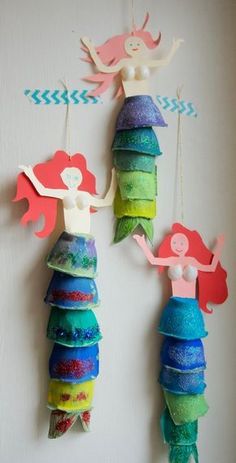 two little mermaids hanging from the side of a wall with paper decorations on them