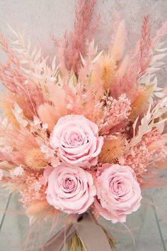 a bouquet of pink flowers and feathers on a white tablecloth with a gray ribbon