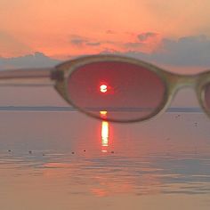 the sun is reflected in some sunglasses on the water's edge as it sets