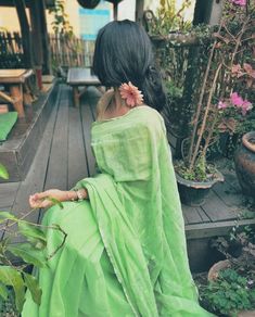 a woman in a green sari sitting on a wooden deck next to potted plants