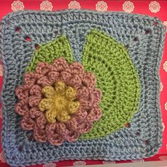 a crocheted square with a flower in the center on a red box top