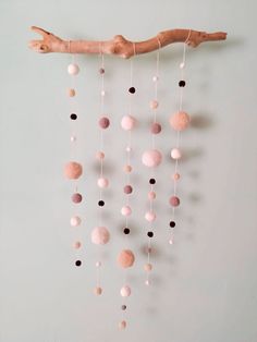 a pink and black mobile hanging on a wall next to a wooden branch with beads