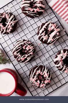 chocolate covered cookies with white and pink sprinkles on a cooling rack next to a cup of milk