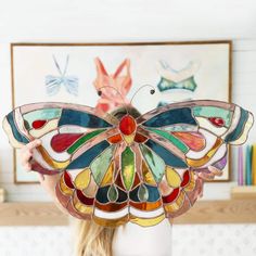 a woman holding up a stained glass butterfly in front of her face with the wings open